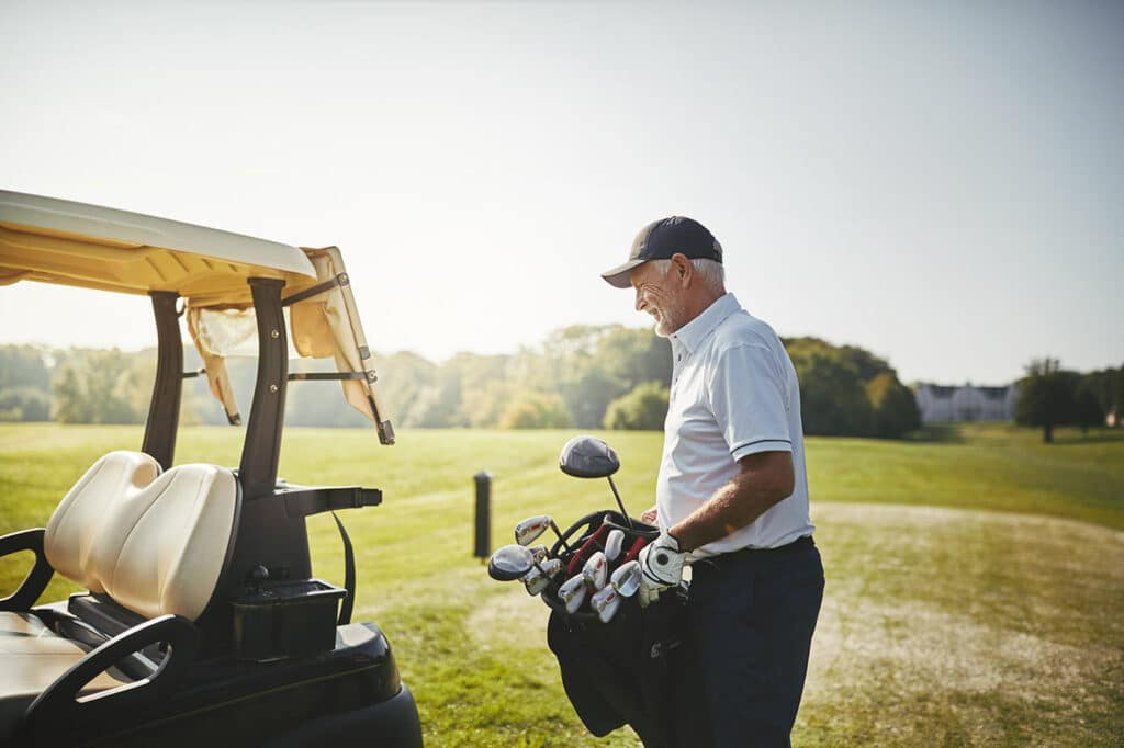 senior man putting his golf club bag in a cart